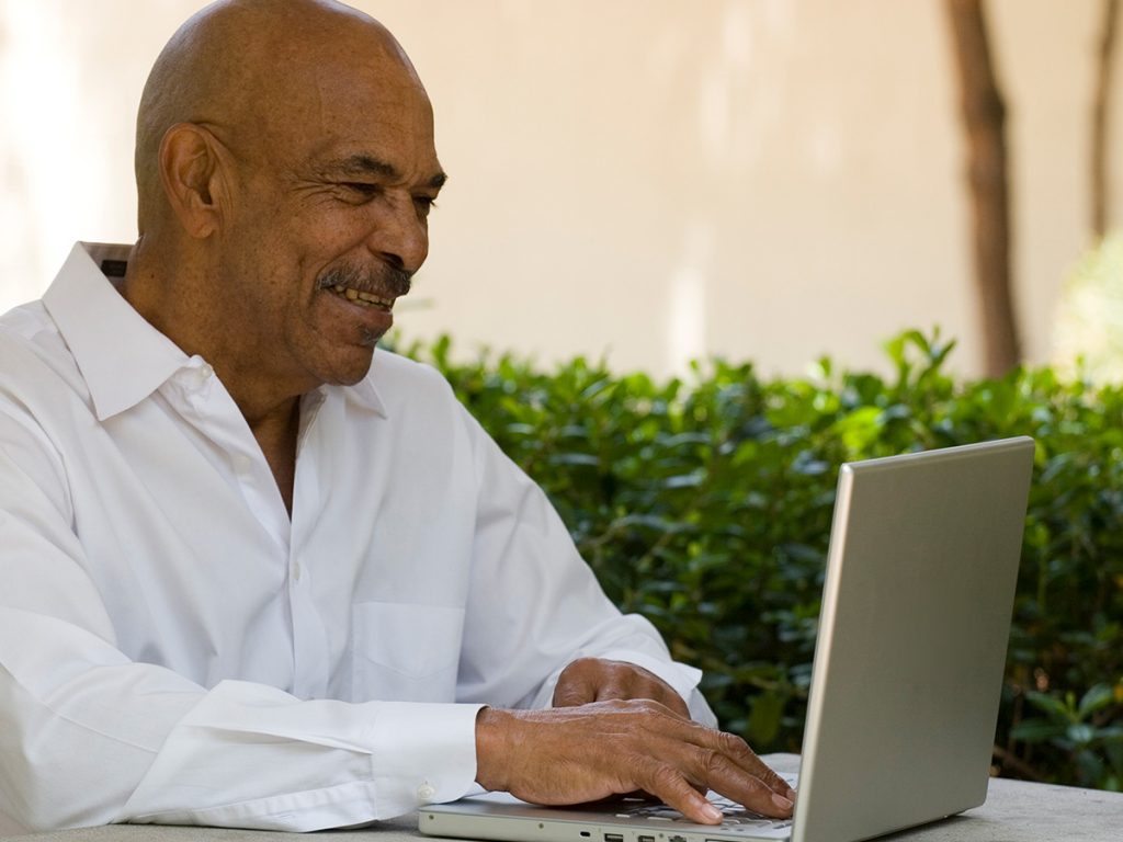 Image of an old man looking at a computer and smiling